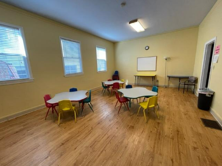 A big room with a white board and three tables, all tables have colorful chairs.