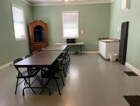 A room with two tables arranged together to make a big table with a basin and a cupboard.